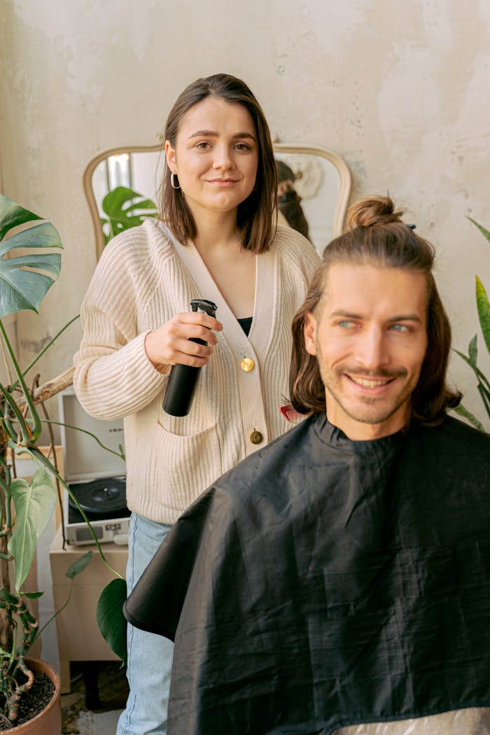A woman styling a man's hair in a cozy, plant-filled salon.