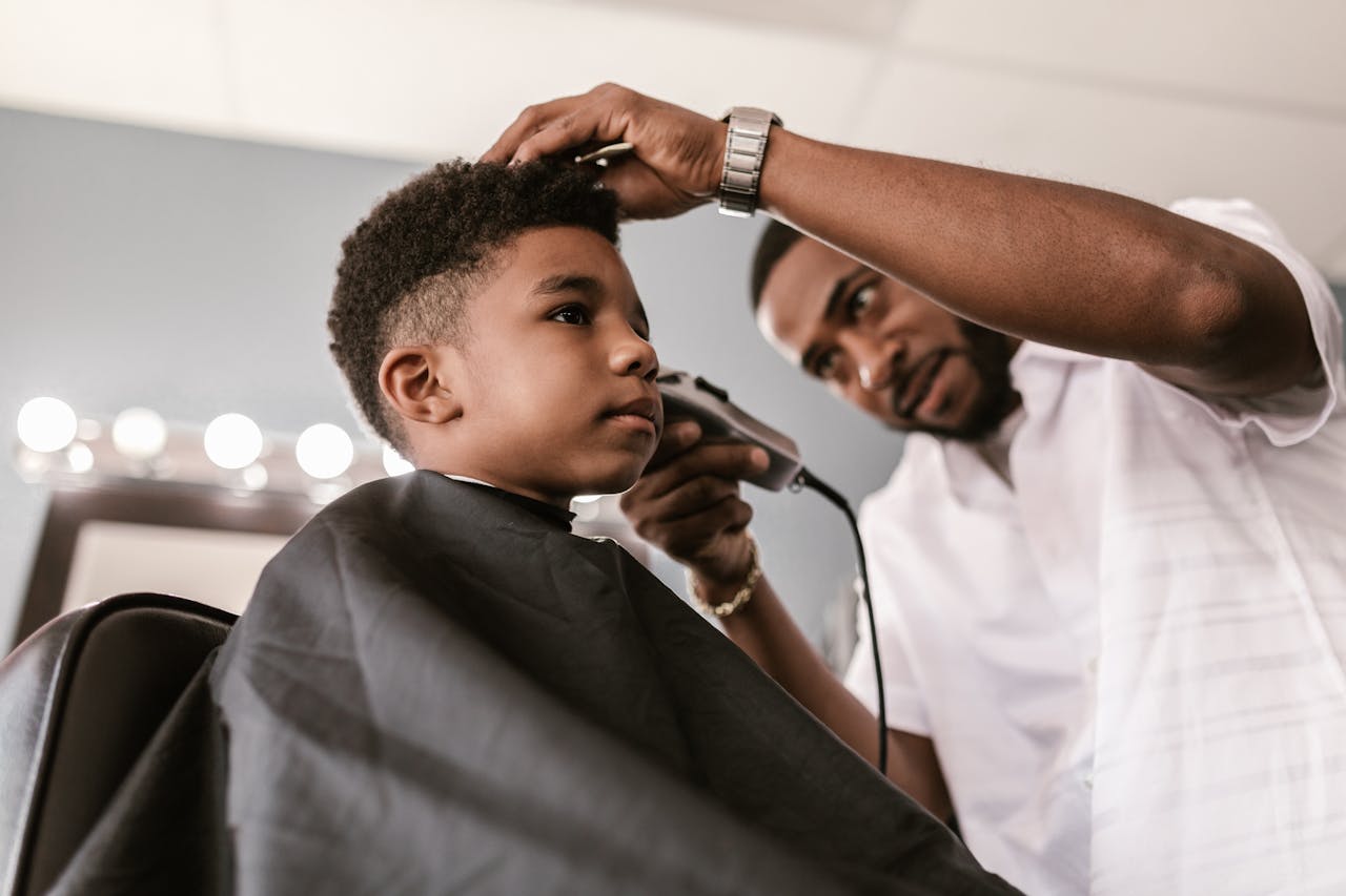 journey A barber skillfully trims a young boy's hair using clippers. Indoor barbershop setting with focus on grooming.