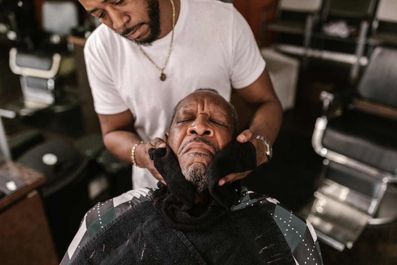 Experienced barber providing grooming service using face towel relaxation technique.